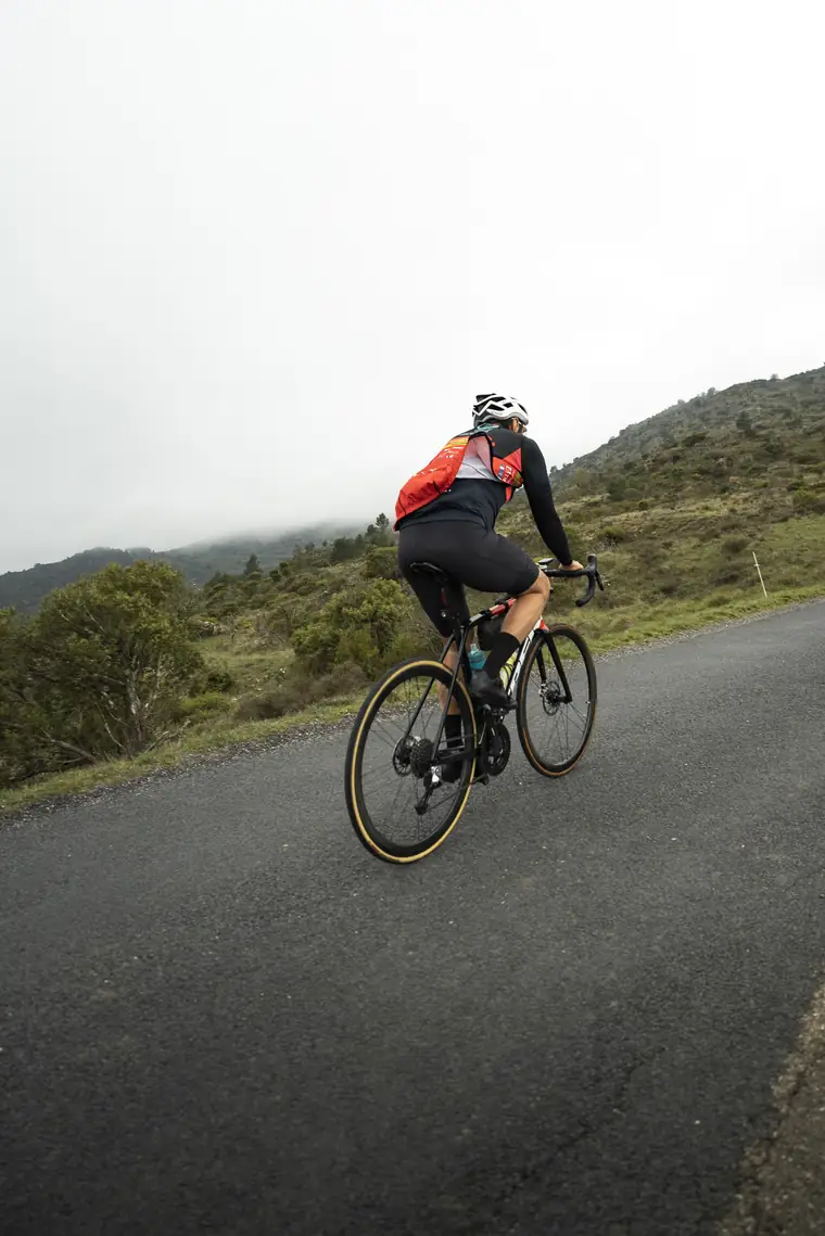 Cycliste de dos qui monte vers un col dans la brume