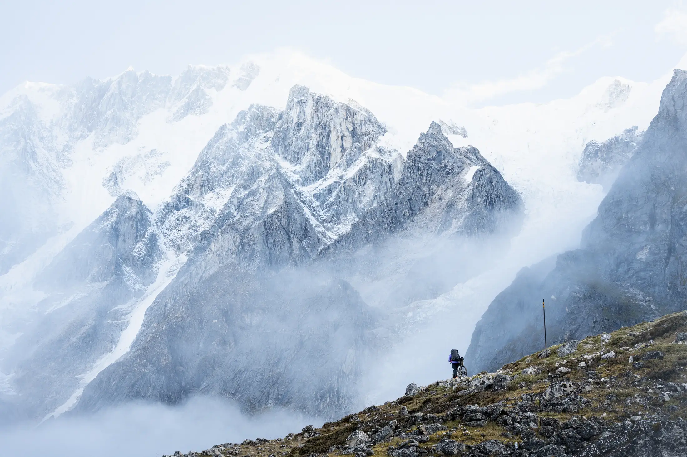 Un cycliste minuscule sur une croupe rocheuse face à une muraille himalayenne enneigée